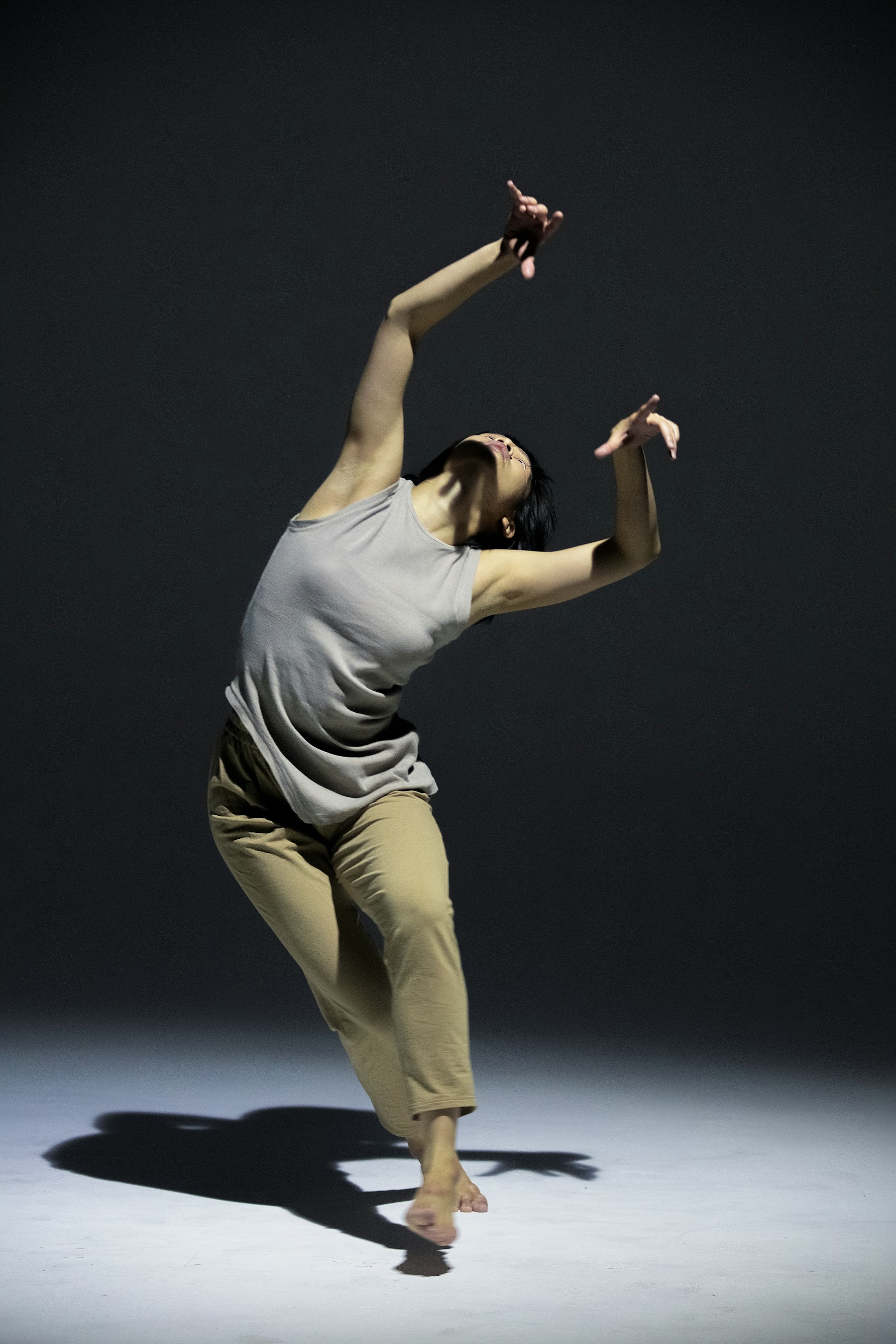 Dancer reaching across a dark rehearsal studio
